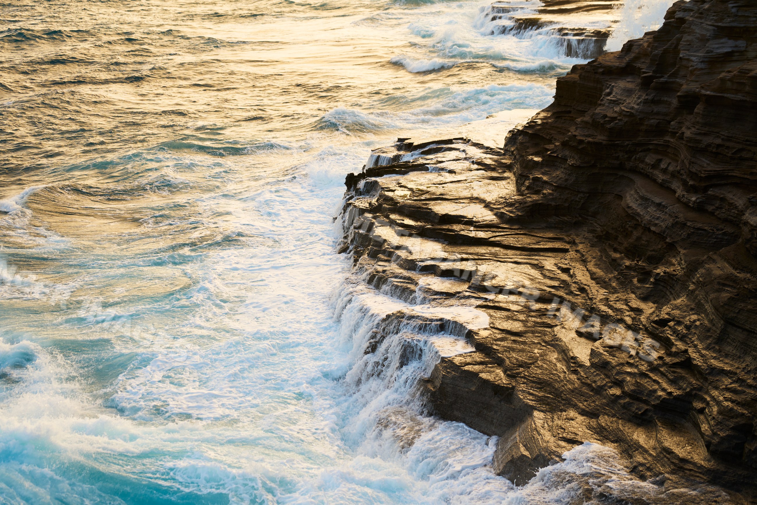 Ocean waves cascading over rocky shoreline at sunset in Oahu Hawaii