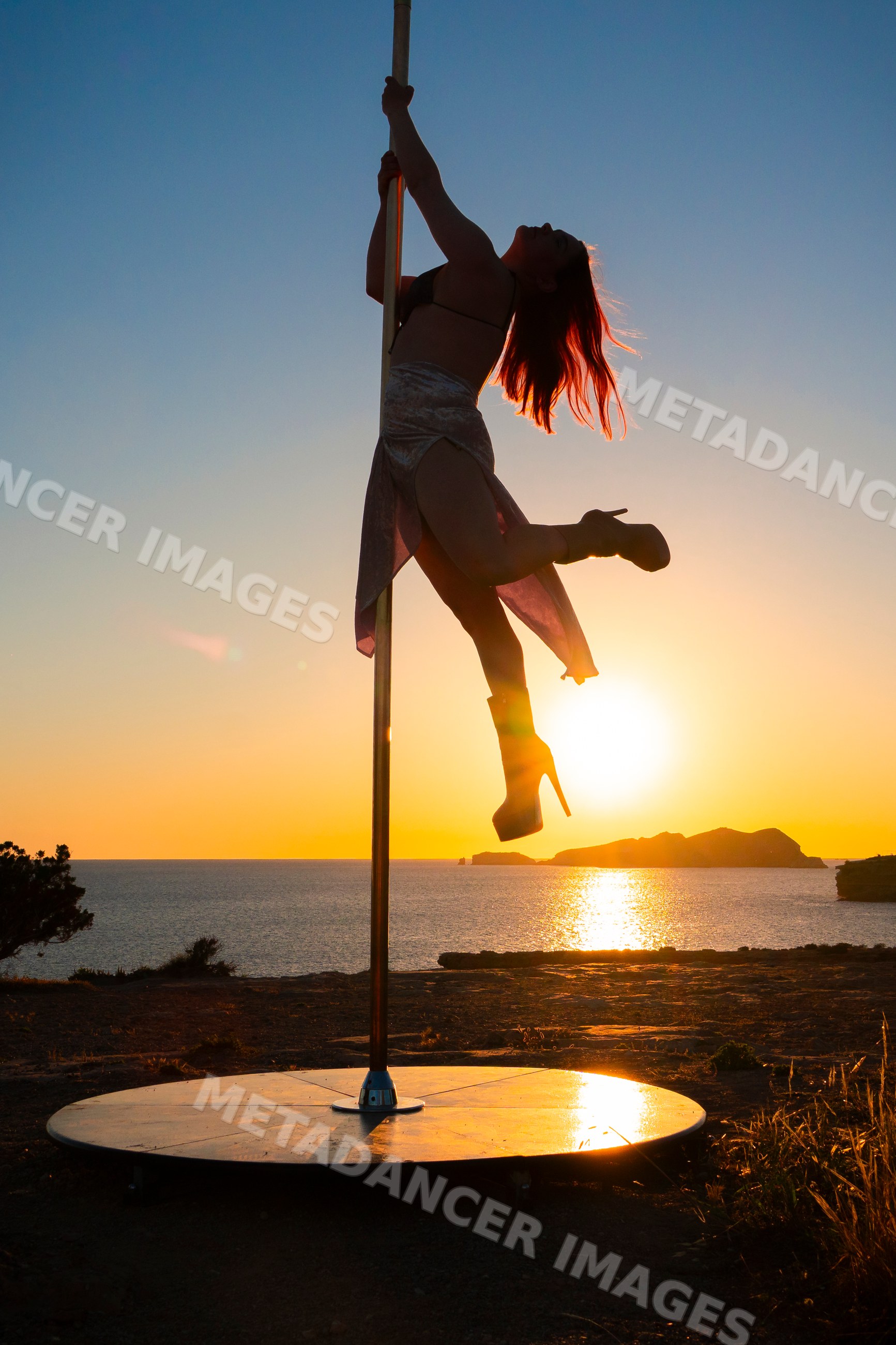 Female Pole Dancer performing at sunset on rocky shore in Ibiza Spain