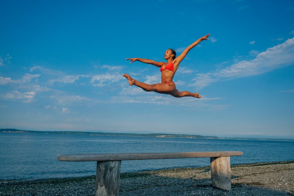 Woman in red swimsuit performing an athletic jump above a bench