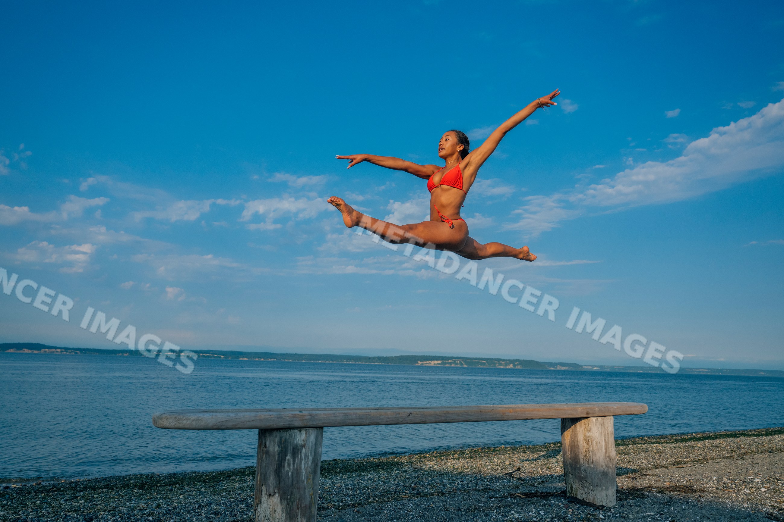 Woman in red swimsuit performing an athletic jump above a bench