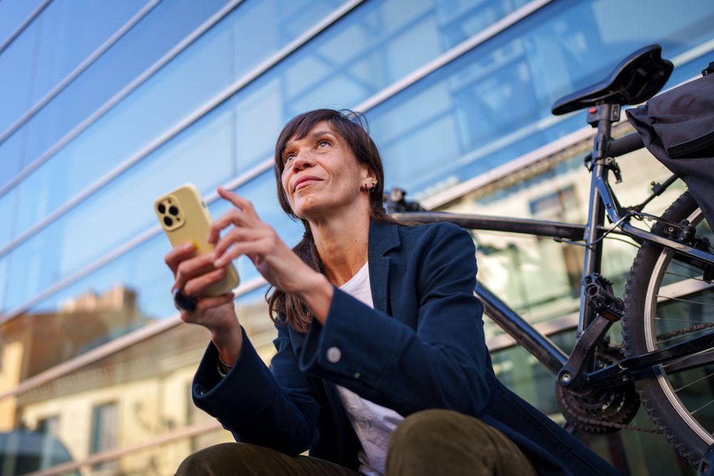 Hispanic woman sitting outside with bicycle using smartphone