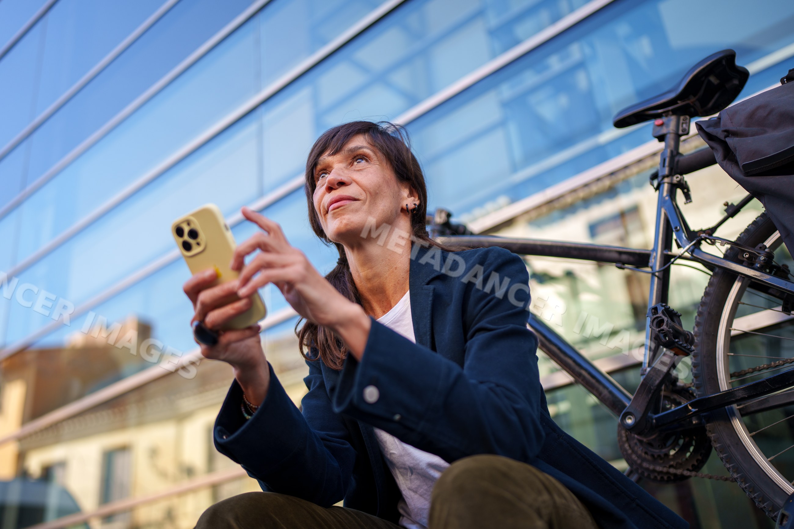 Hispanic woman sitting outside with bicycle using smartphone