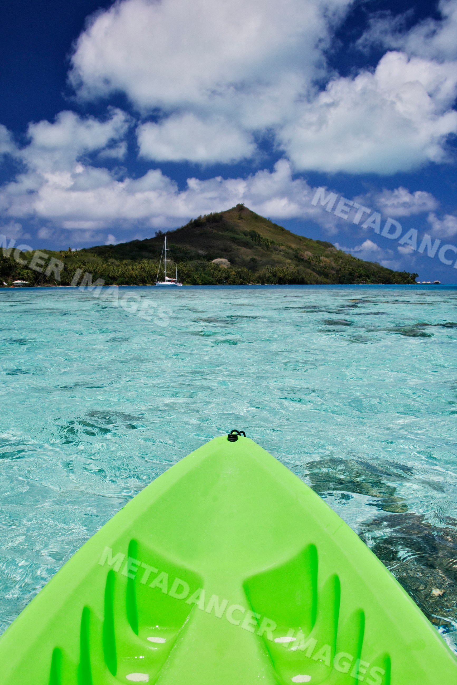 Green kayak on clear lagoon waters toward tropical island hill french
