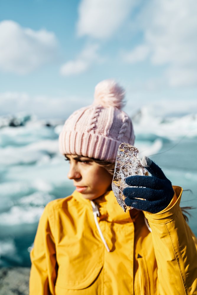 A white woman holds ice near a frozen lake in Iceland during winter