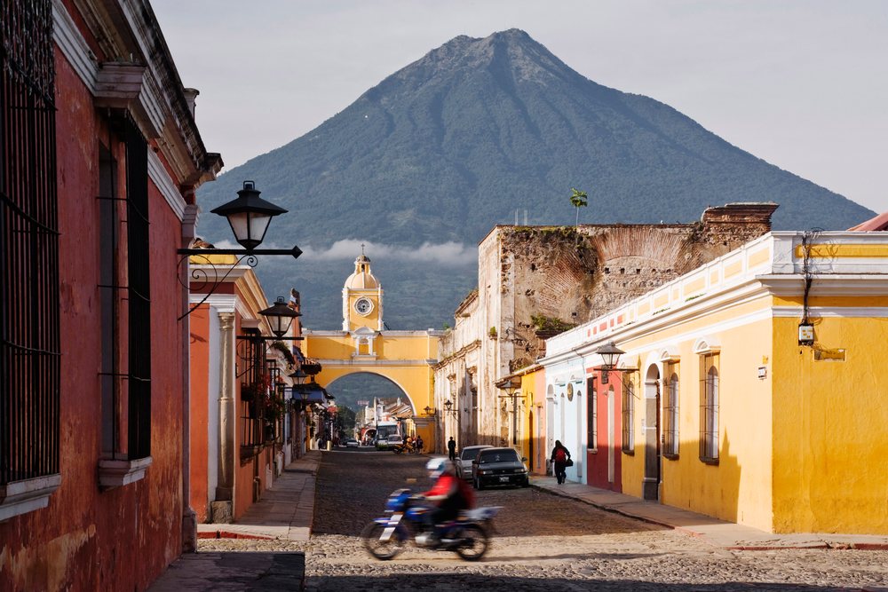 Agua volcano behind a historic cobblestone street and arch clock tower