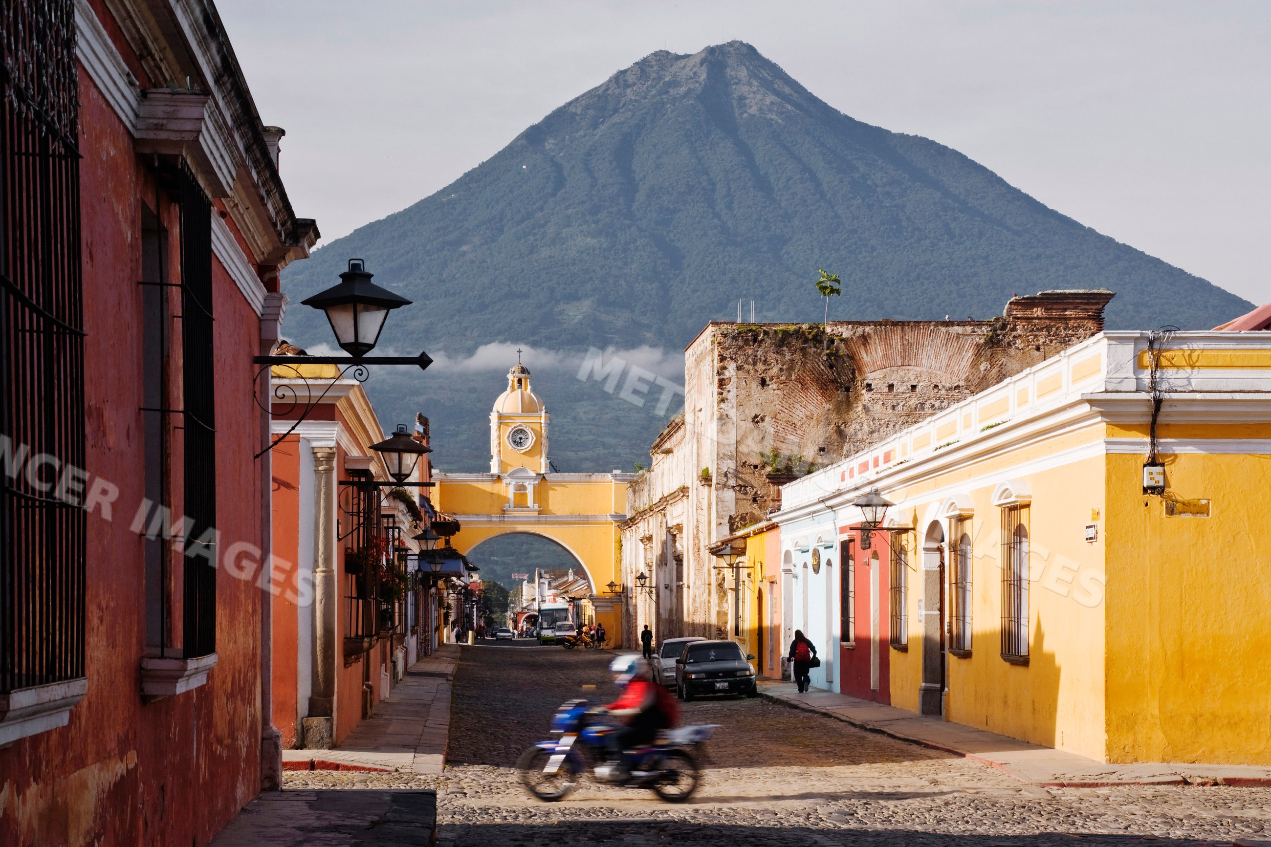 Agua volcano behind a historic cobblestone street and arch clock tower
