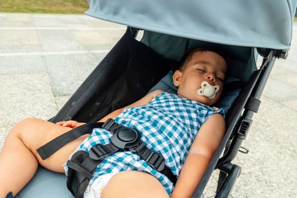Sleeping baby resting in stroller outdoors with pacifier