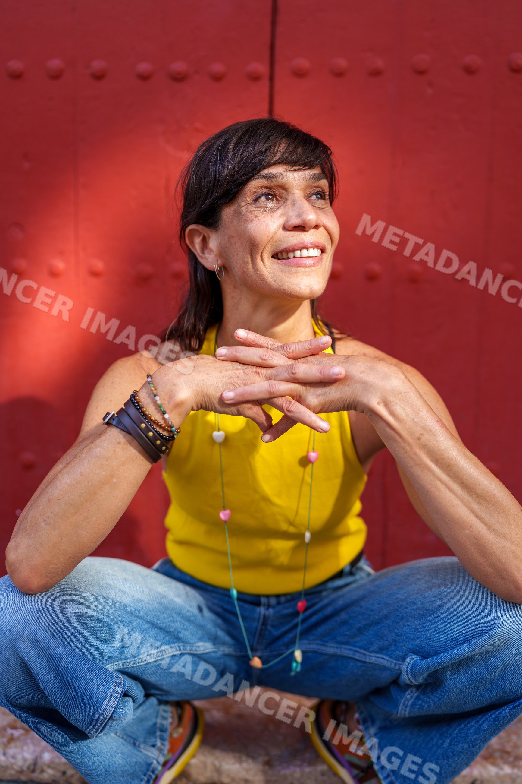 Hispanic woman sitting in yellow top and blue jeans by red wall
