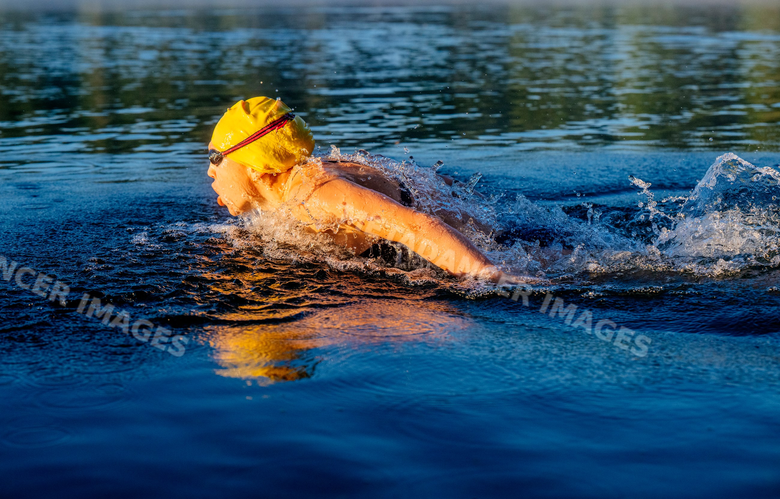 White swimmer with yellow cap swimming freestyle in open water lake