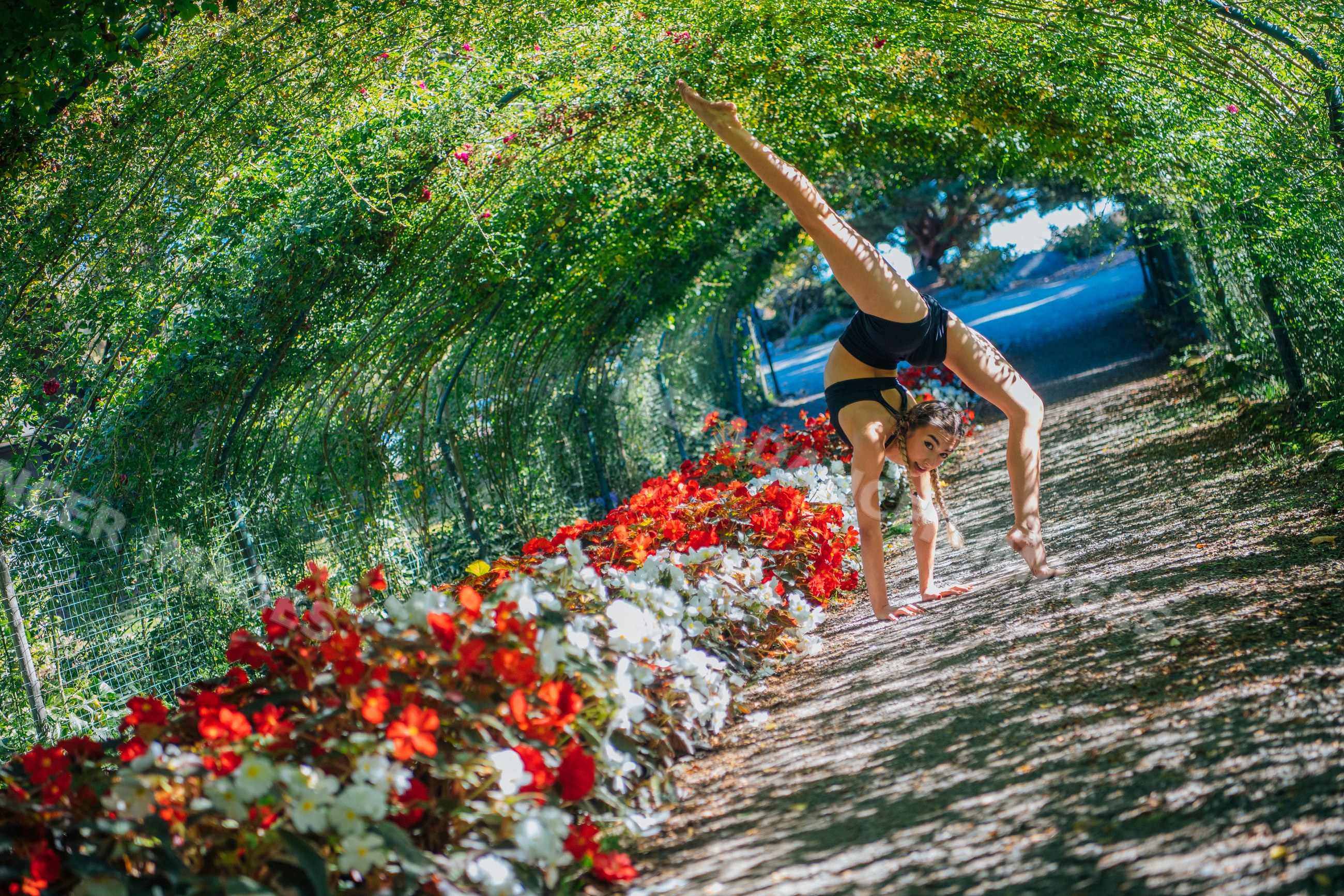 Contortionist performing handstand in flower-lined garden tunnel