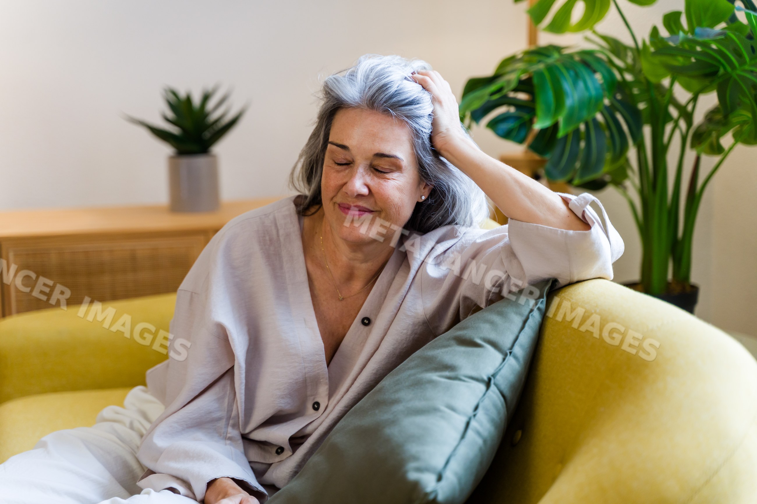 White woman with gray hair relaxing on yellow sofa in home interior
