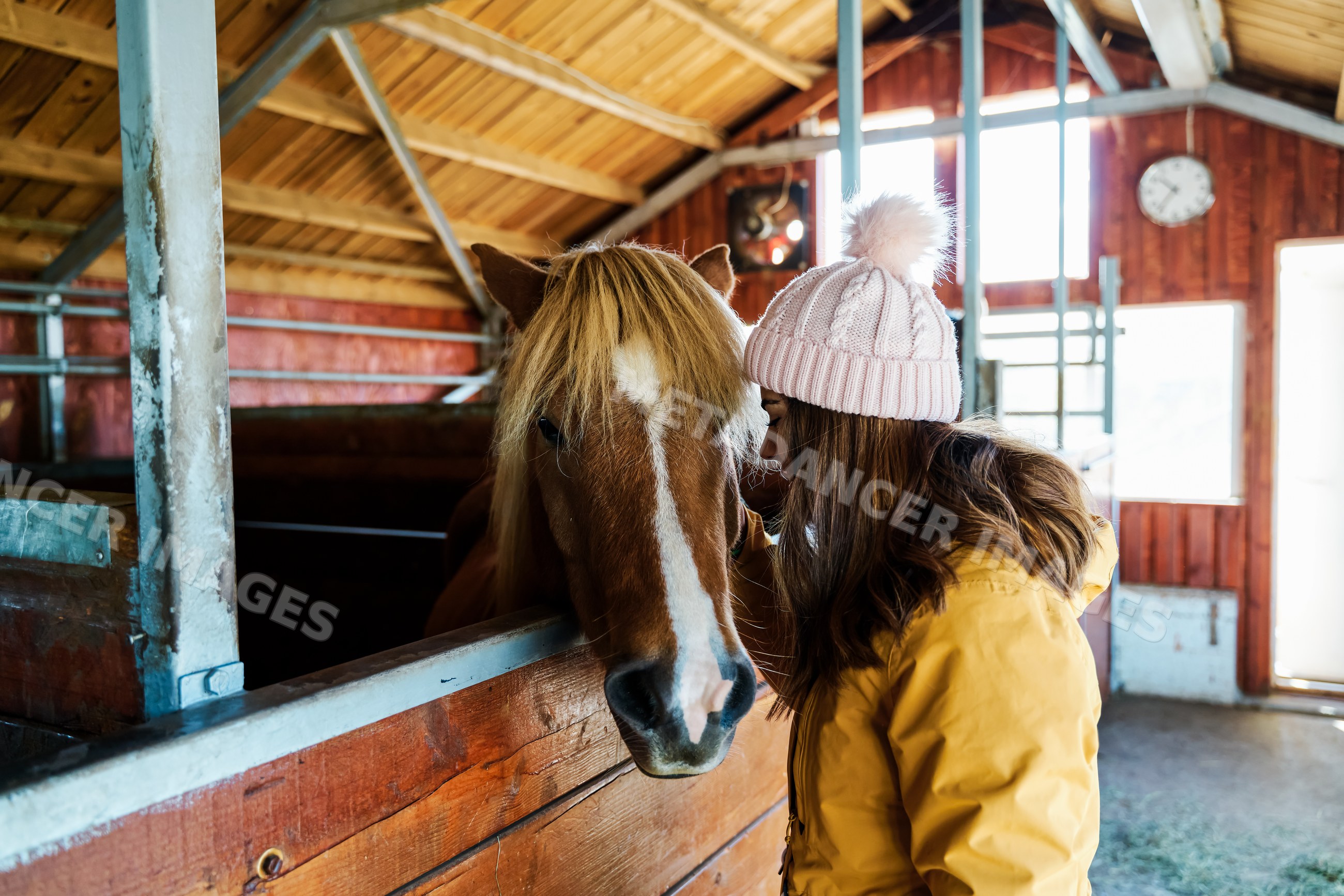 A white woman gently pets a brown horse inside a wooden stable
