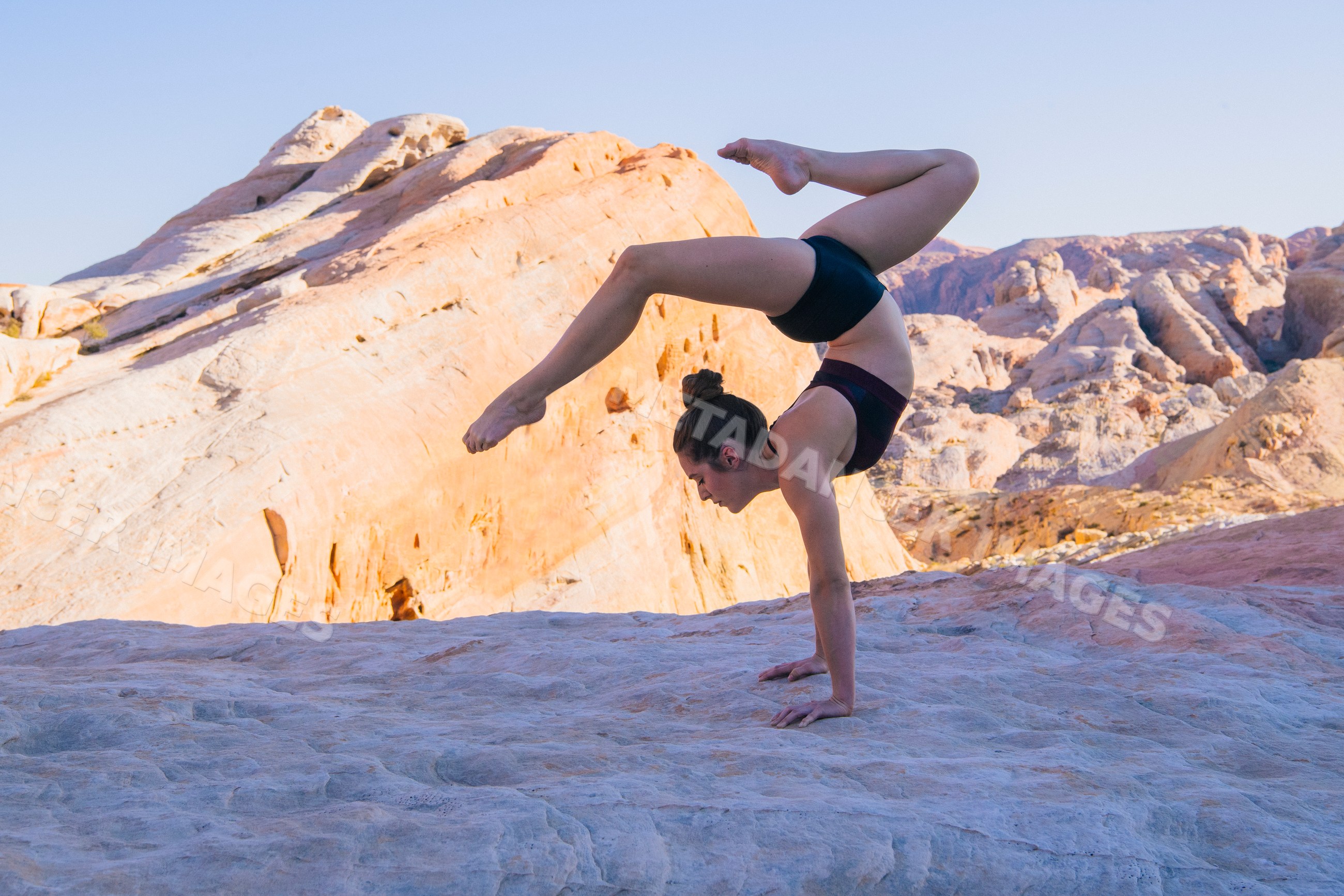 White woman holding handstand yoga pose on rocky desert terrain