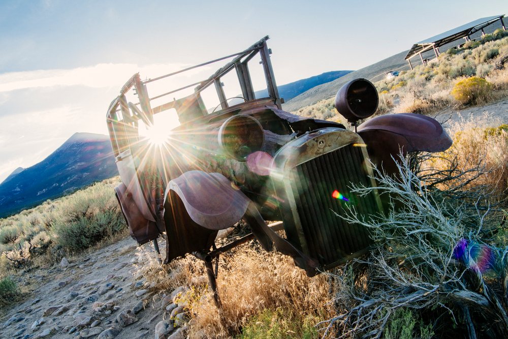Rusty car wreck surrounded by desert brush and mountains