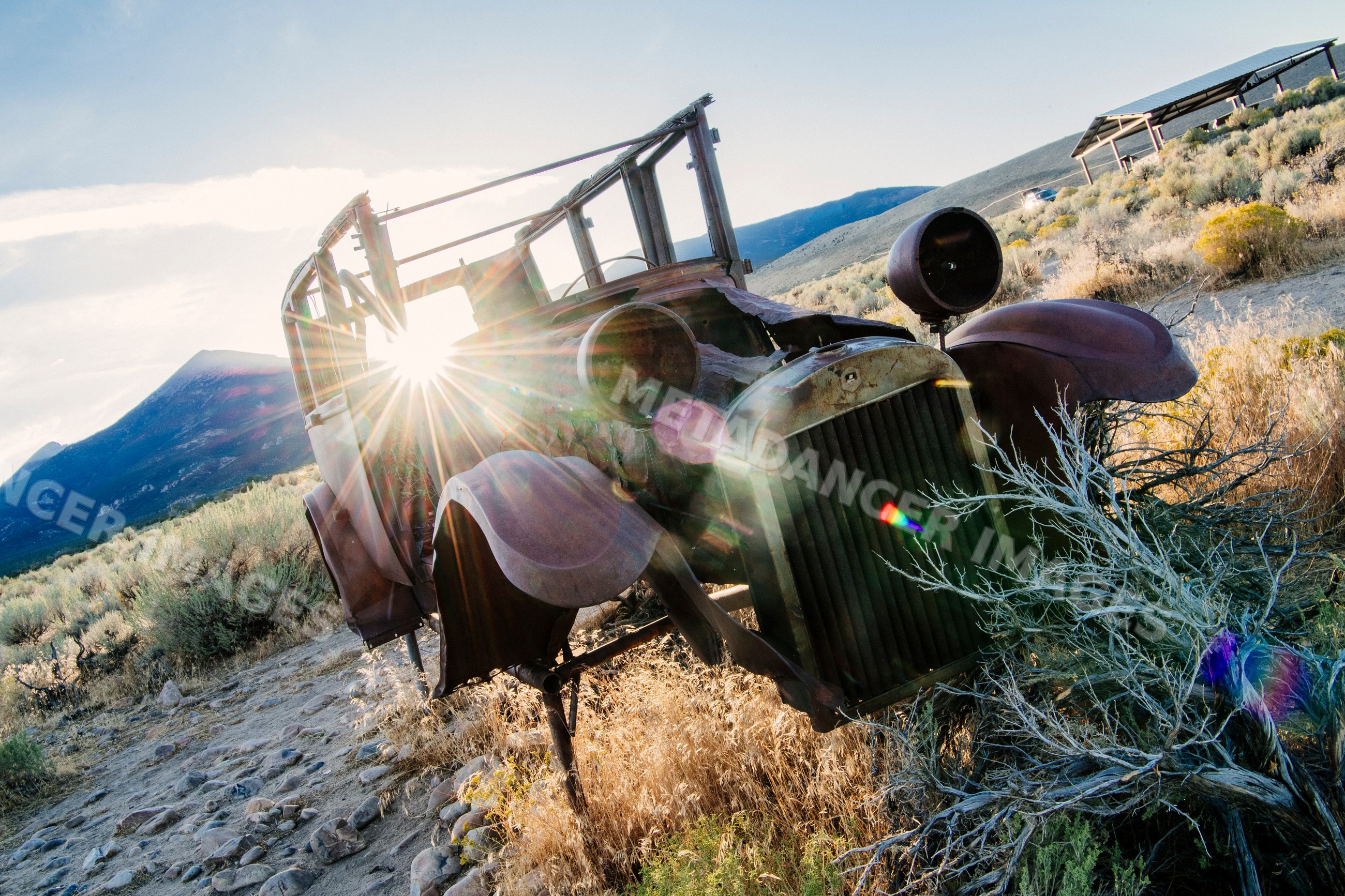 Rusty car wreck surrounded by desert brush and mountains