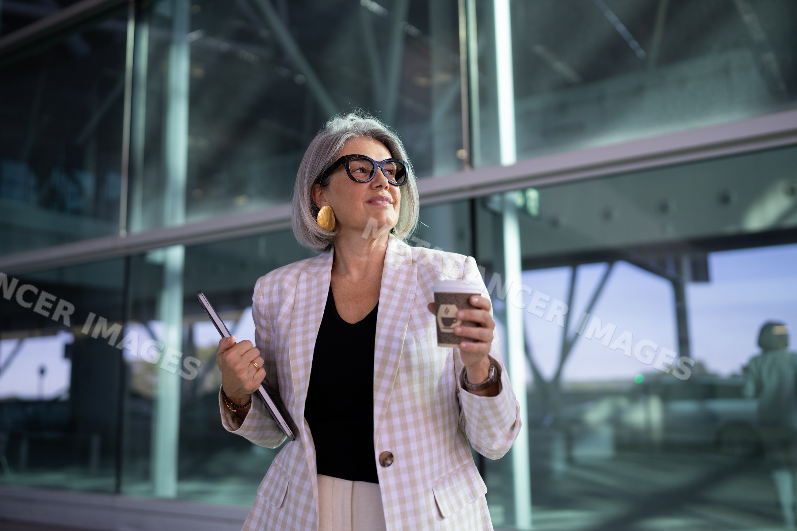 Businesswoman holding coffee cup and tablet outside modern office