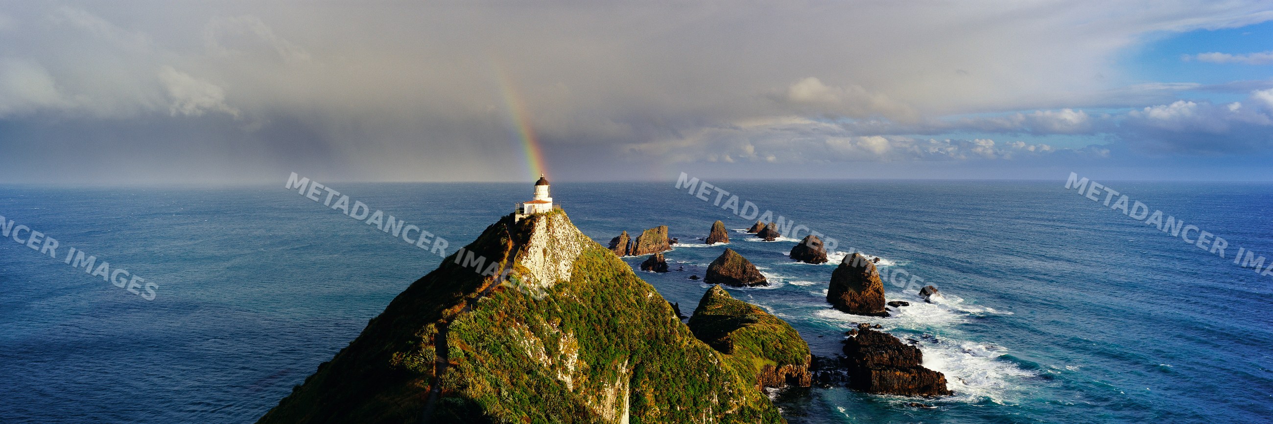 Lighthouse with rainbow over rocky ocean coastline