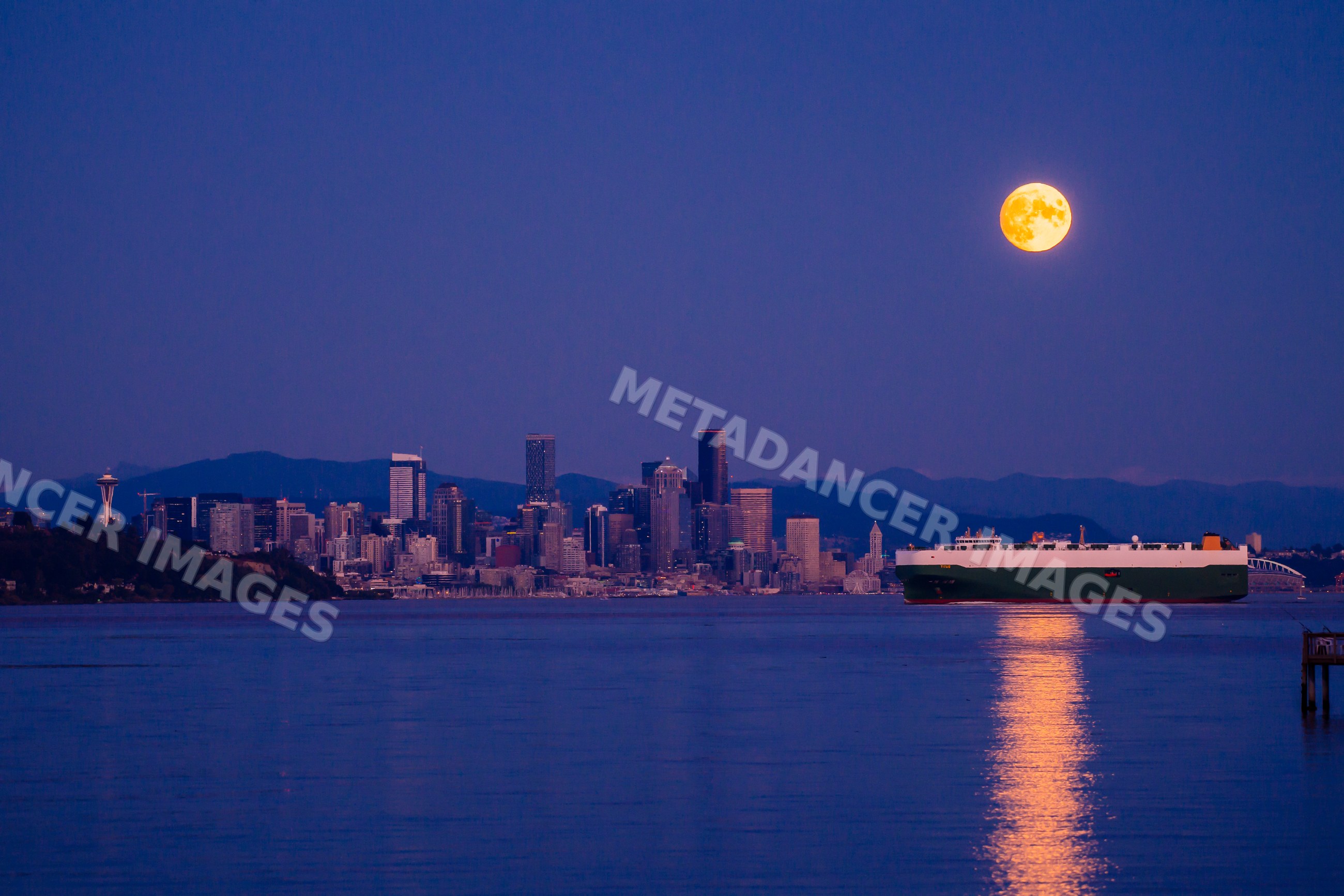 Full moon over Seattle skyline with cargo ship on waterfront