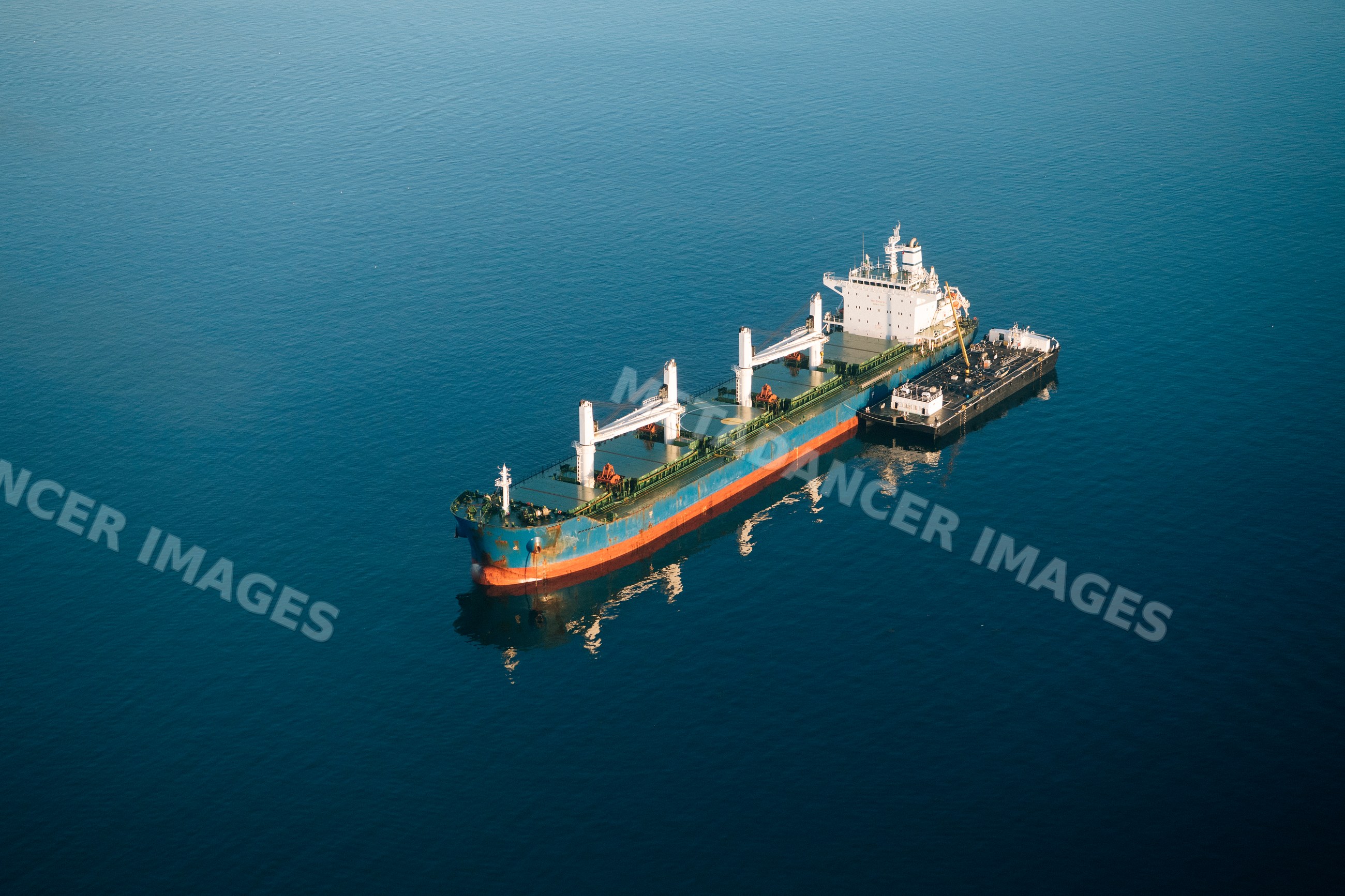 Cargo ship being refueled by tanker vessel in a beach