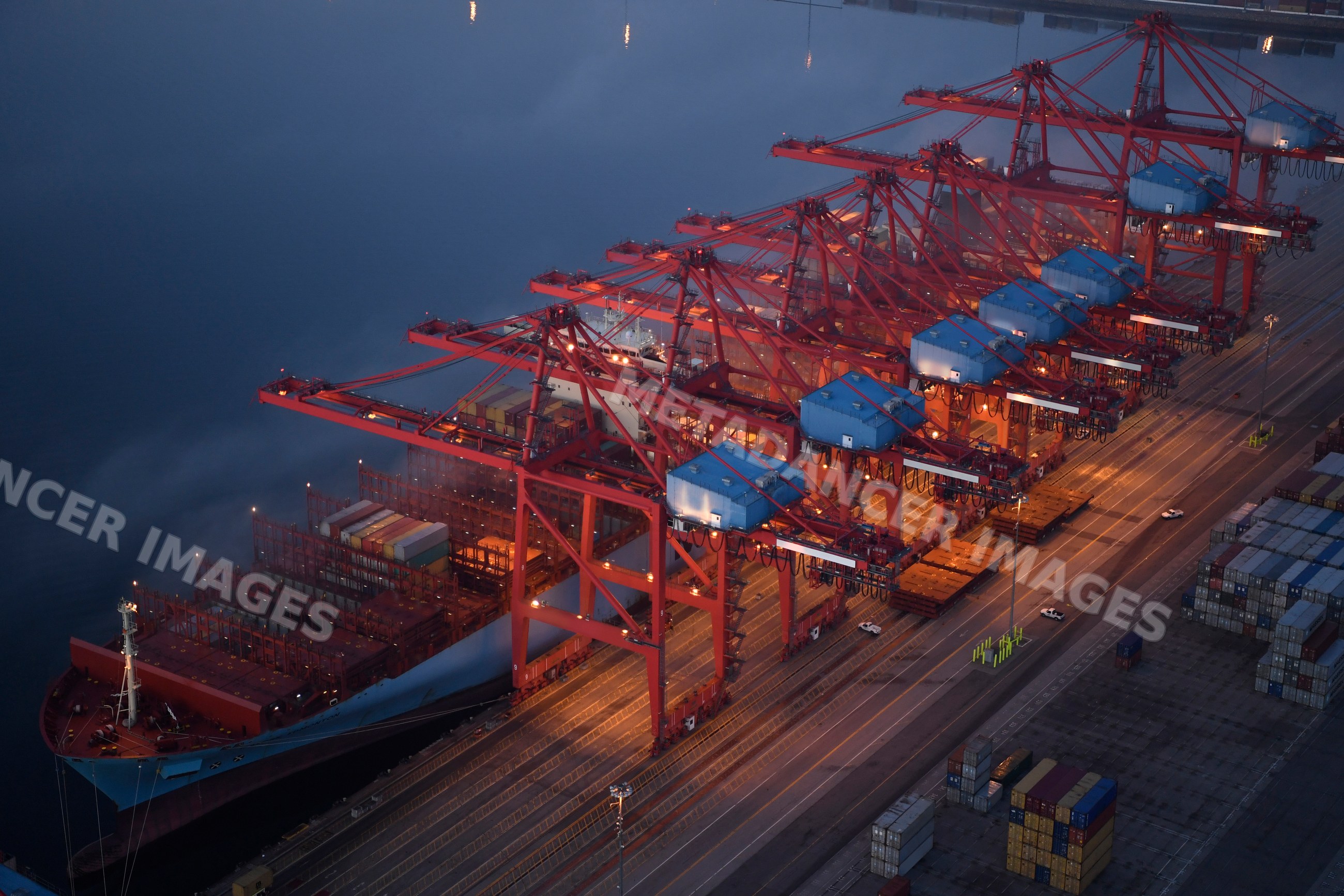 A container ship is loaded with cargo containers at port cranes