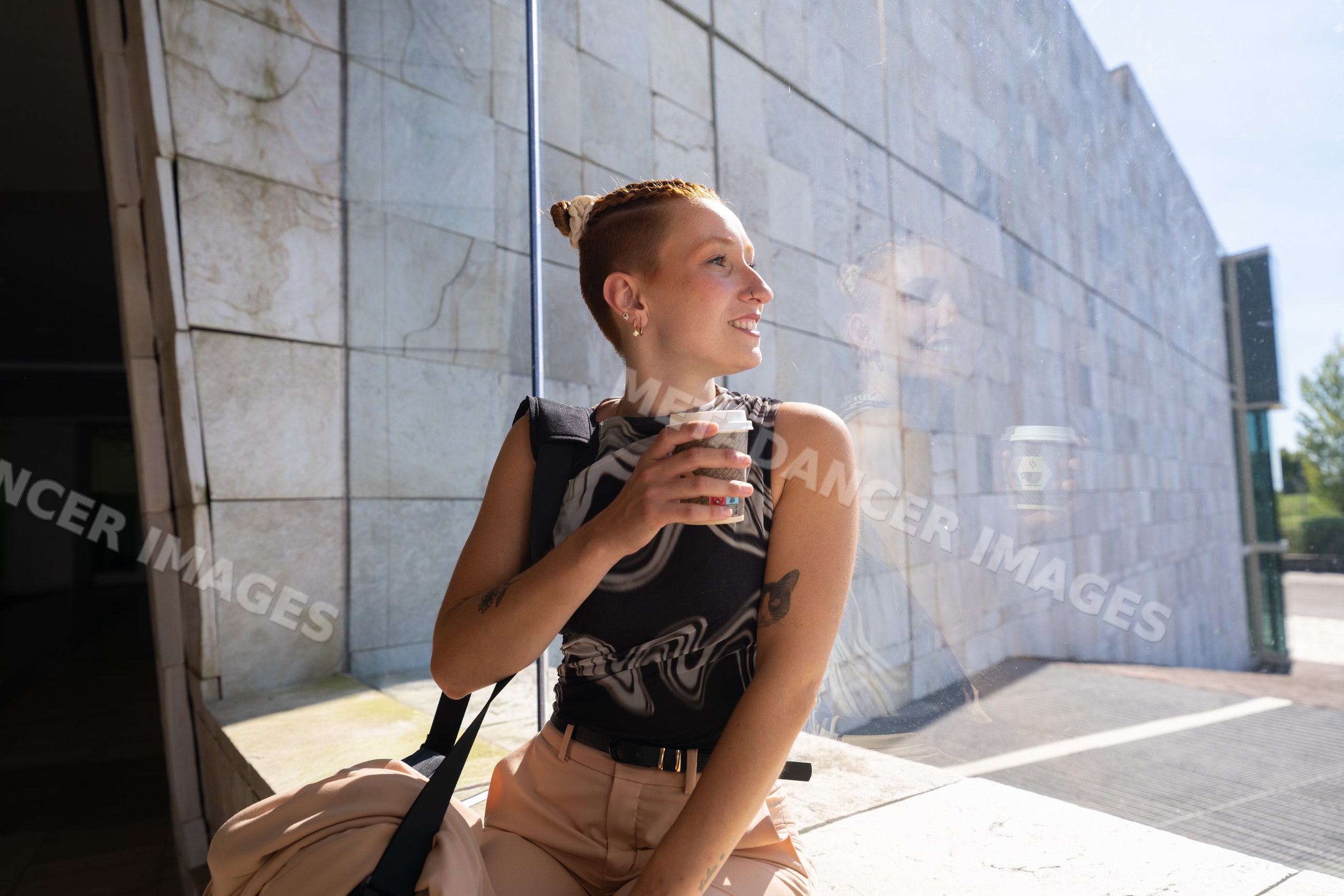 Young white woman holding coffee cup sitting by window outdoors