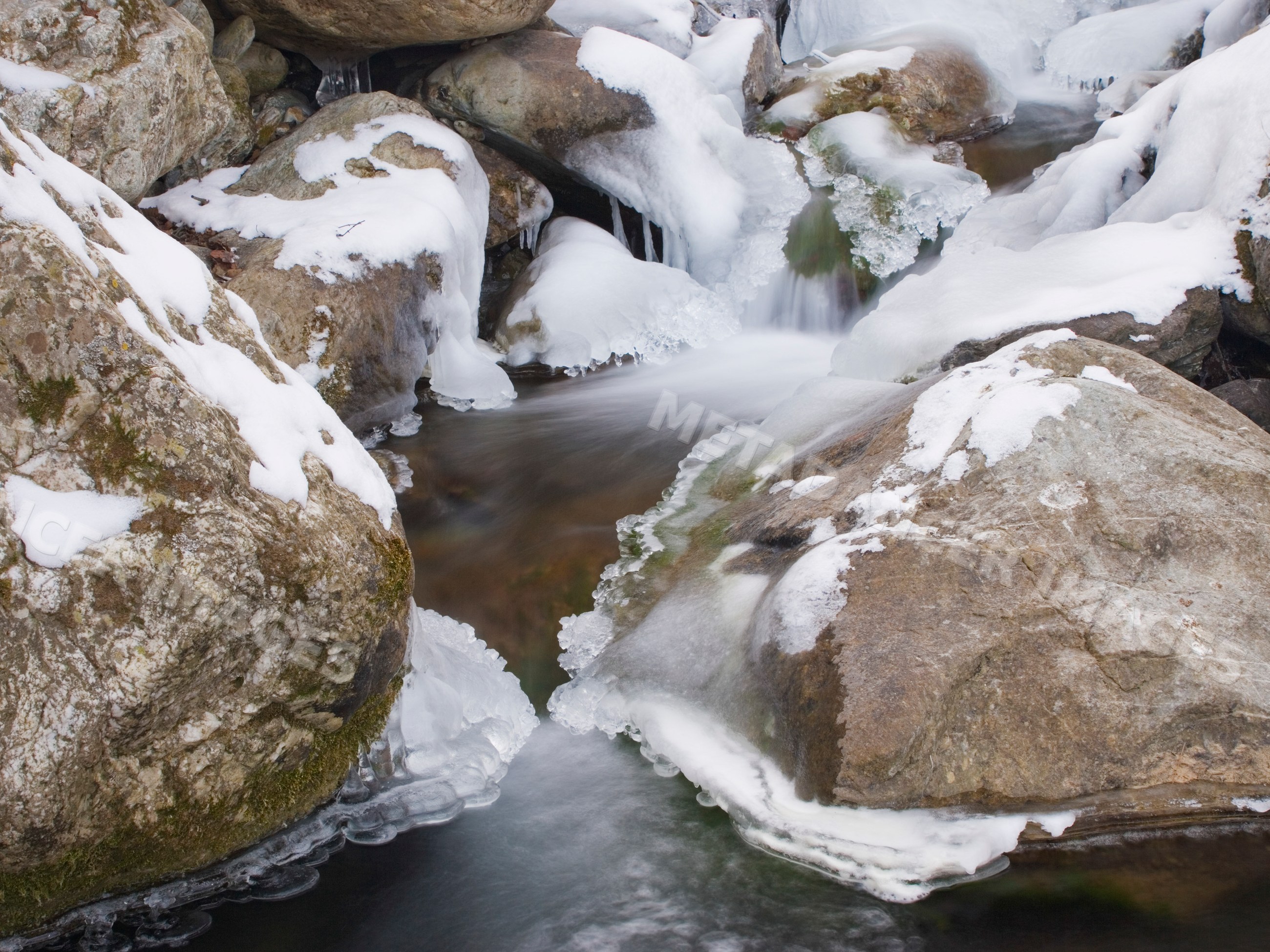 Stream flowing through snow-covered rocks in japan