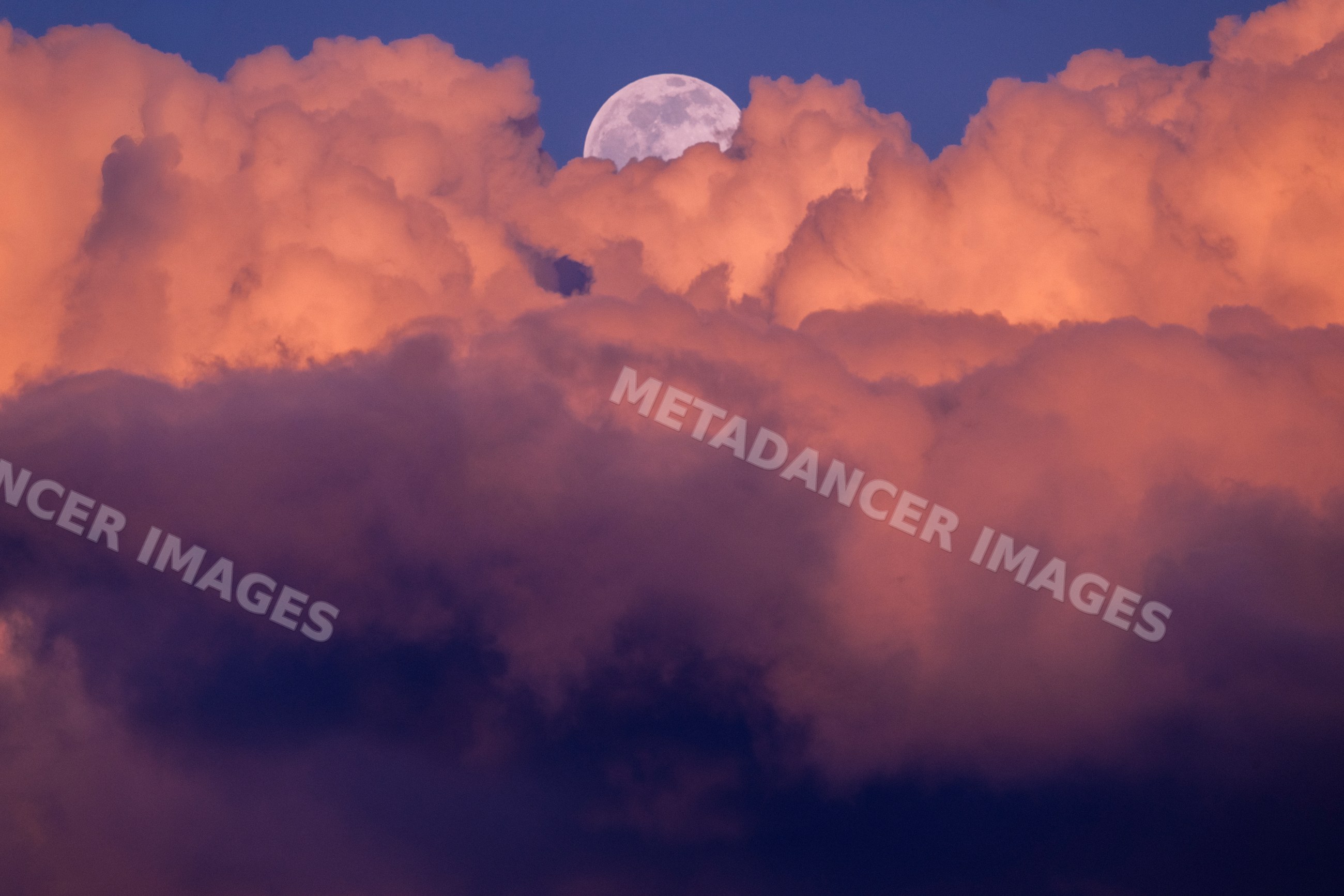 Full moon rising behind orange clouds at twilight over Seattle