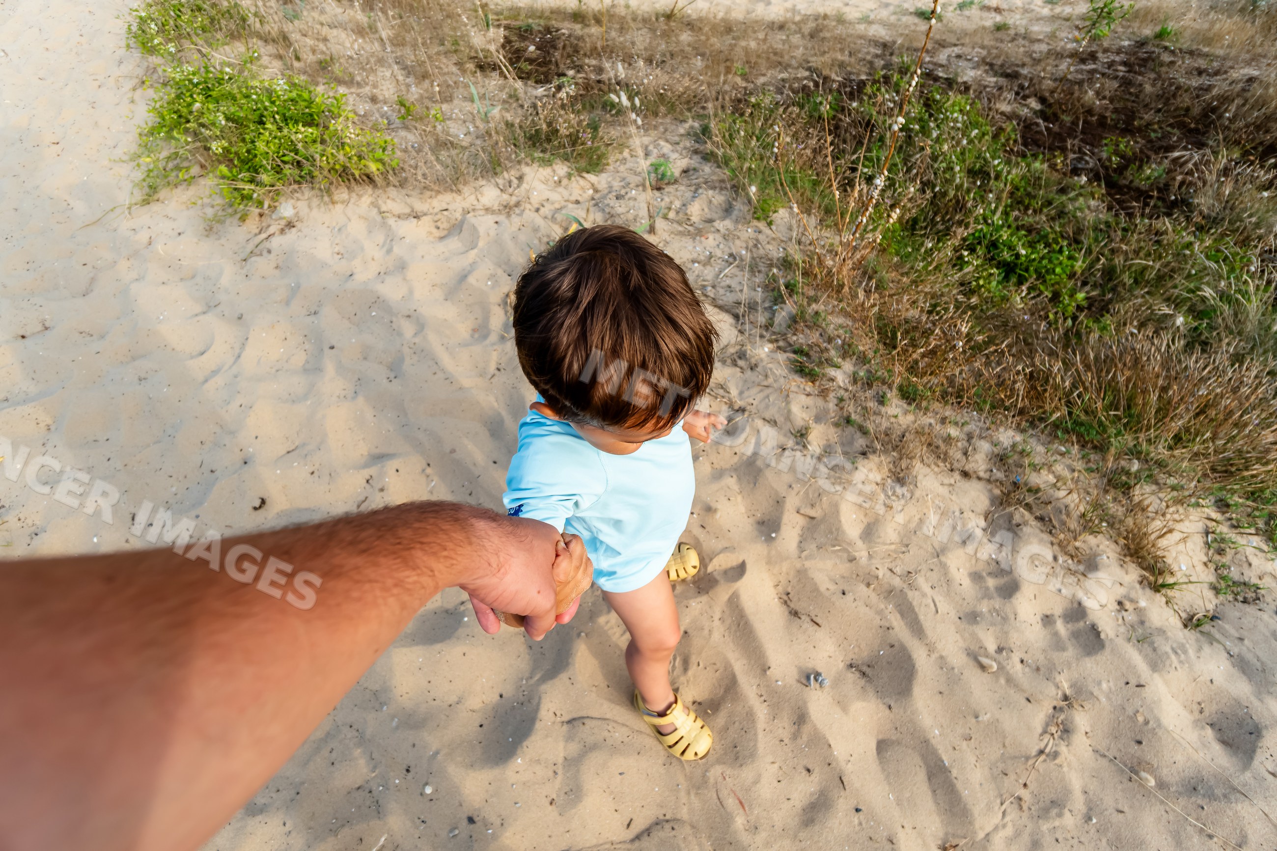 White child walking on sand holding adult's hand outdoors