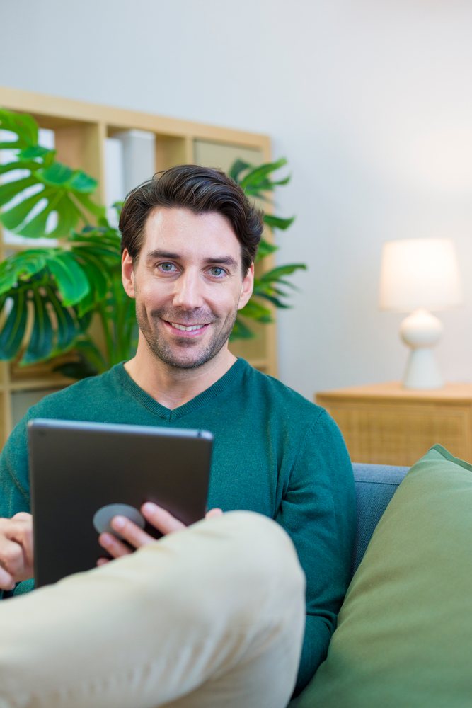 White man using tablet sitting on couch in home living room