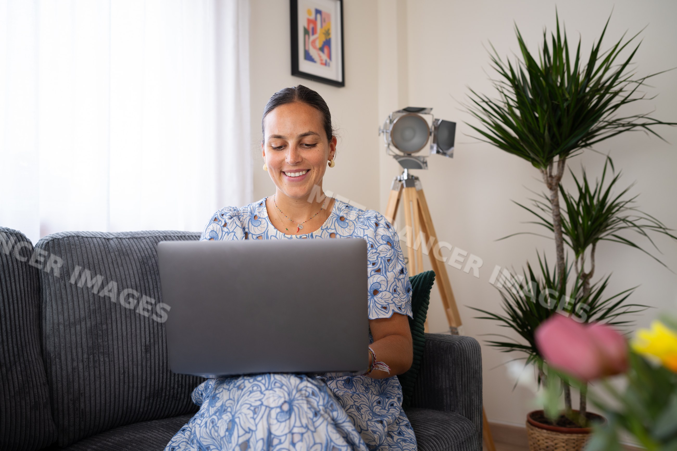 White woman working on laptop indoors on sofa