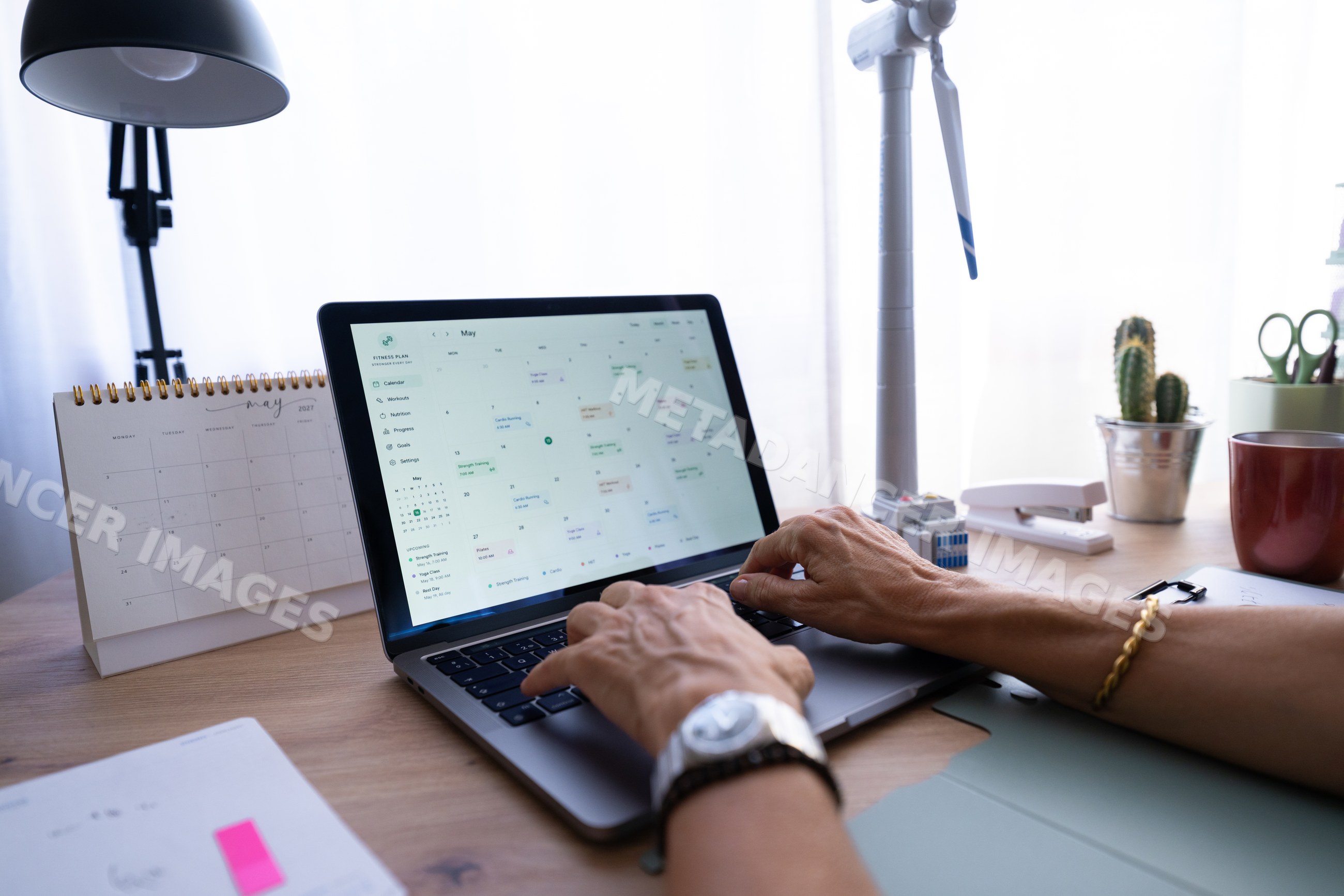 Hands typing on laptop with digital calendar on desk in home office