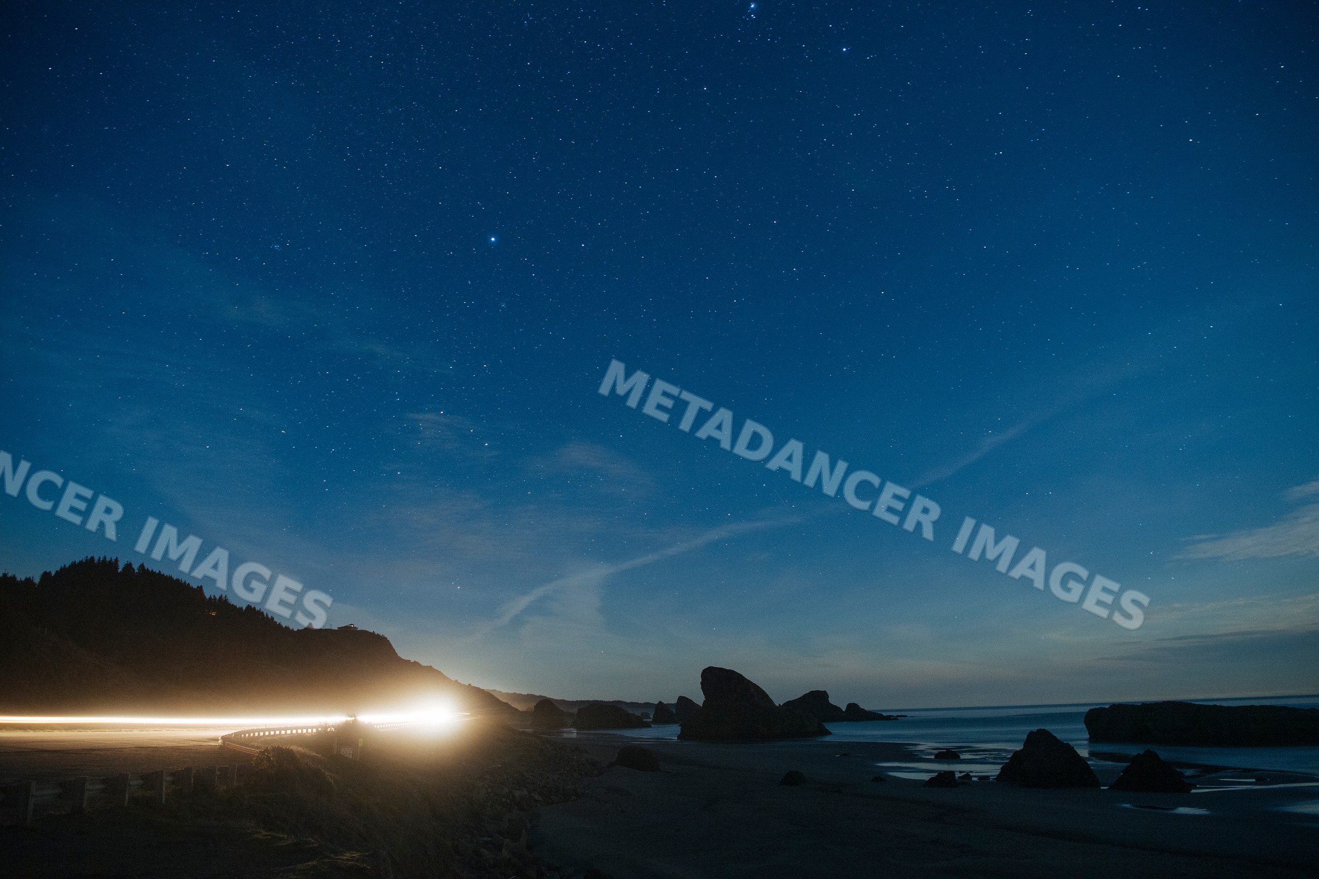 Night sky with stars over rocky coast and highway with car headlights