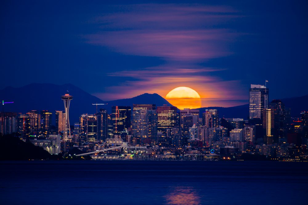 Seattle skyline with moonrise behind mountains at night