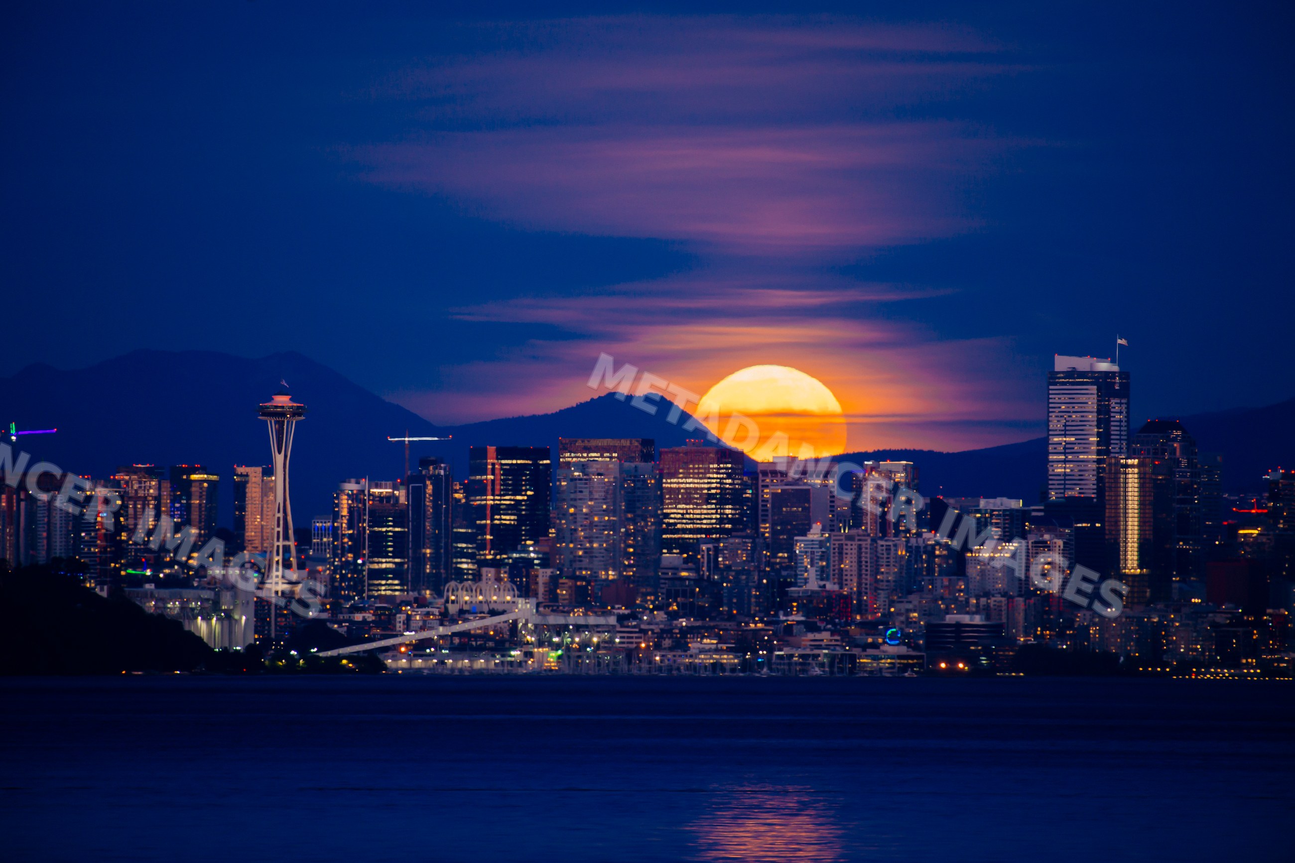 Seattle skyline with moonrise behind mountains at night