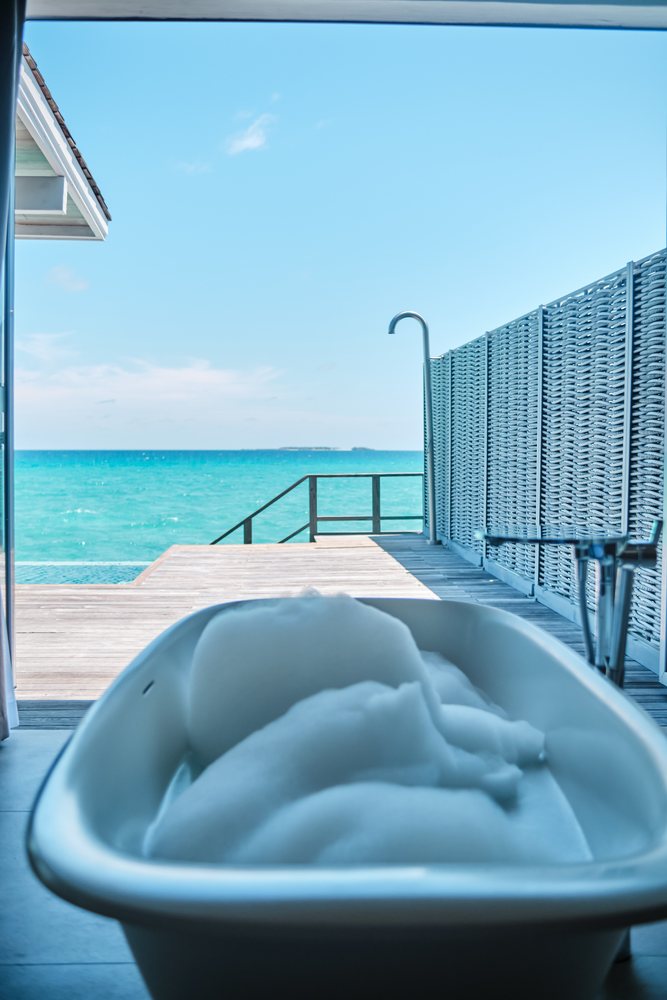 Bathtub with foam opens onto a deck beside the ocean