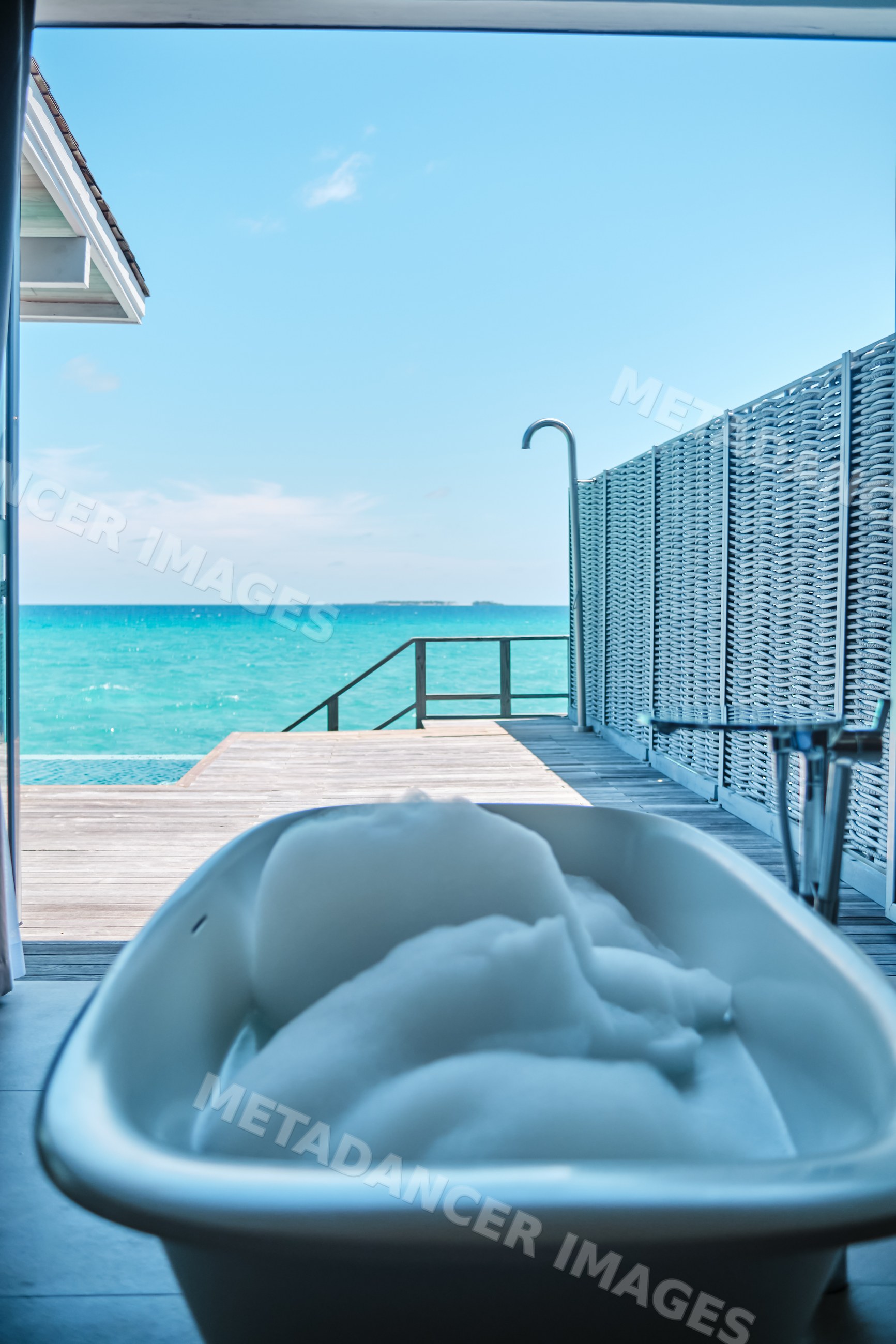 Bathtub with foam opens onto a deck beside the ocean