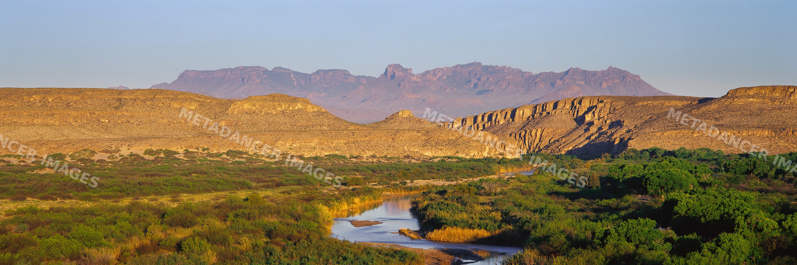 Desert river valley with mountains and vegetation in sunlight
