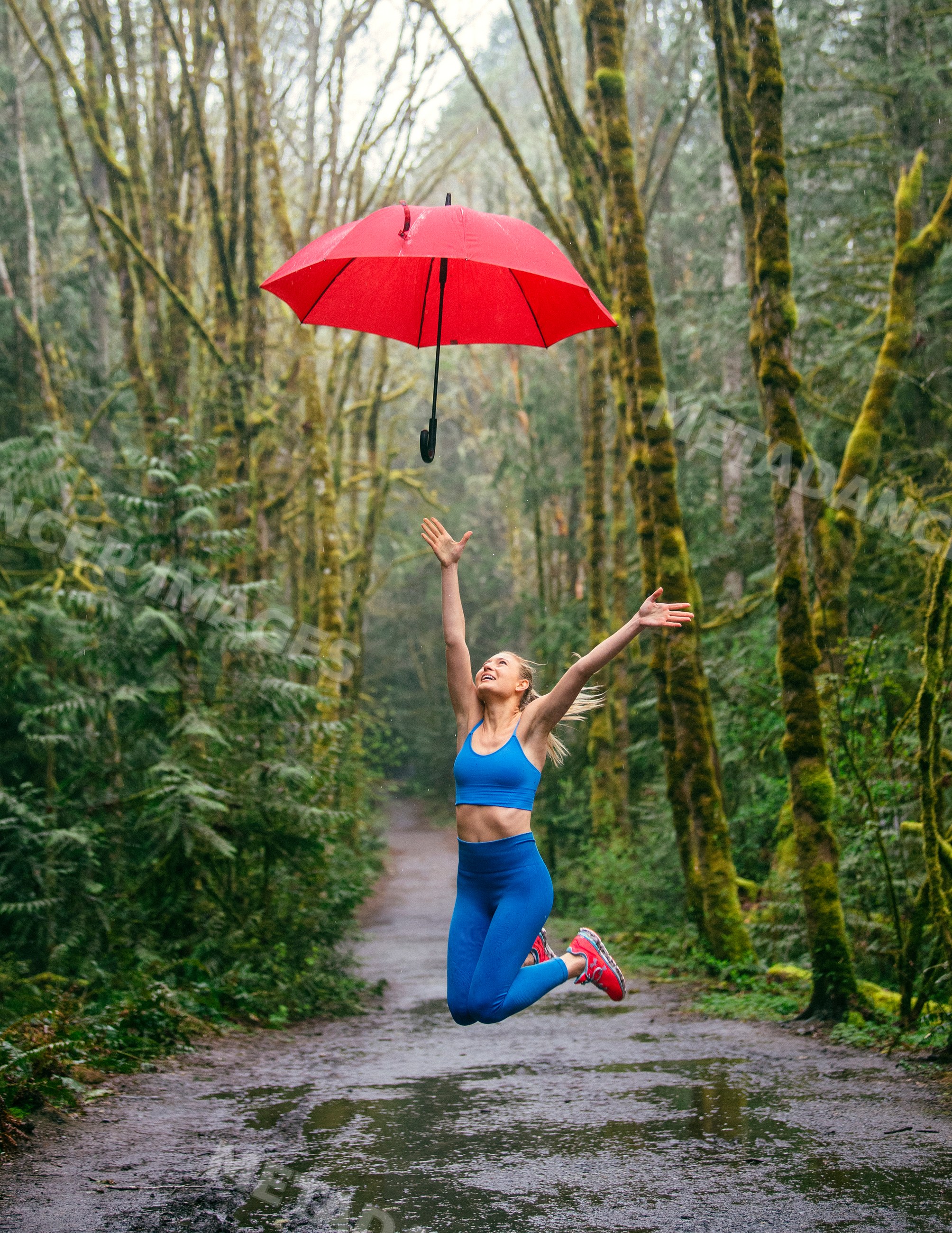 White woman jumping with red umbrella on wet forest path