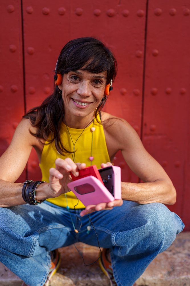 Hispanic woman holds a cassette tape player sitting near a red wall