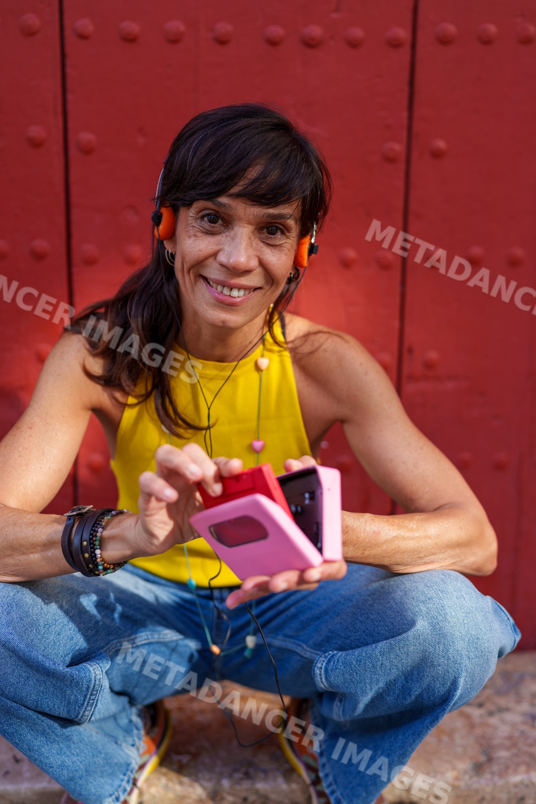 Hispanic woman holds a cassette tape player sitting near a red wall