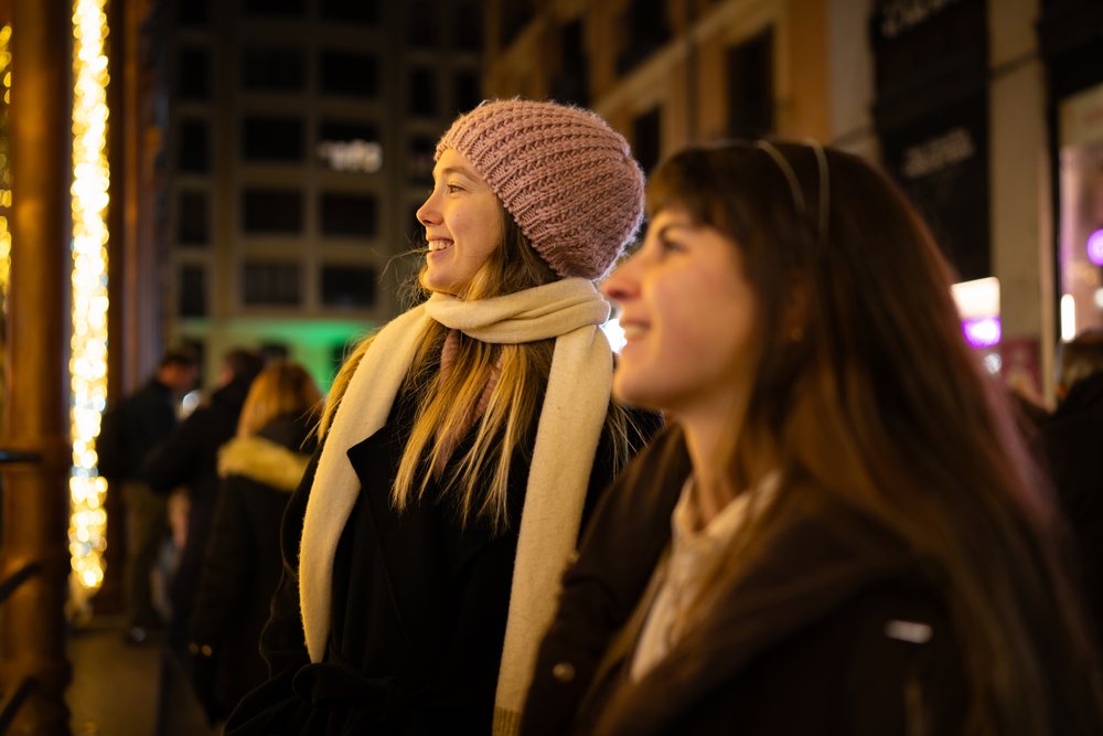 Two white women smiling outdoors at night in winter clothing in Madrid