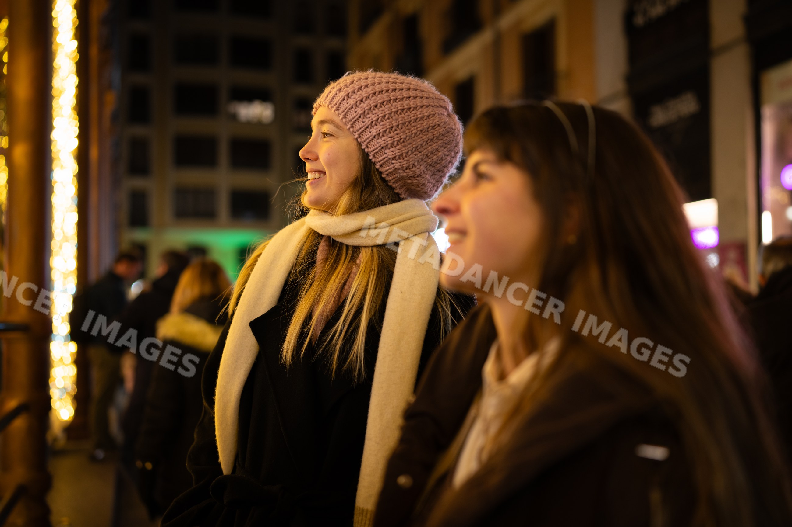 Two white women smiling outdoors at night in winter clothing in Madrid