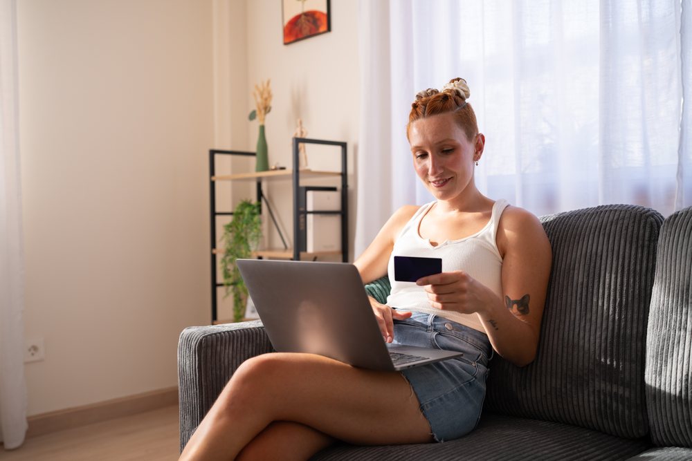A white woman shops online at home using a credit card and laptop