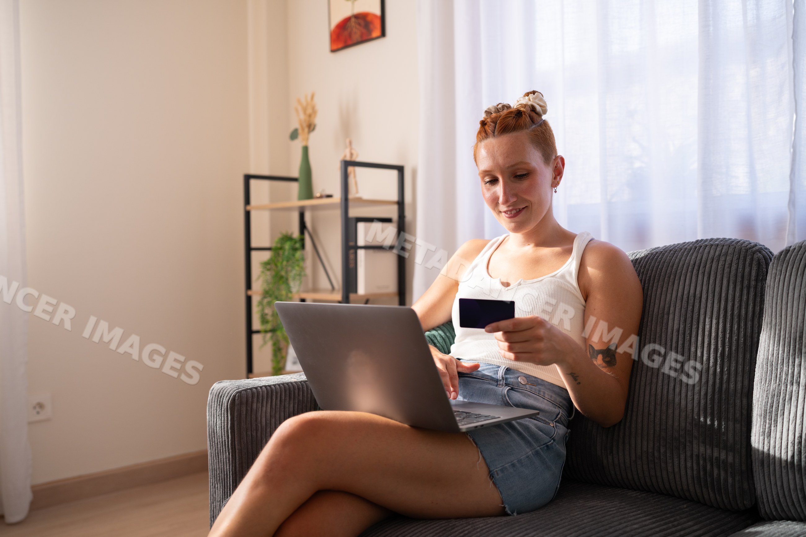 A white woman shops online at home using a credit card and laptop