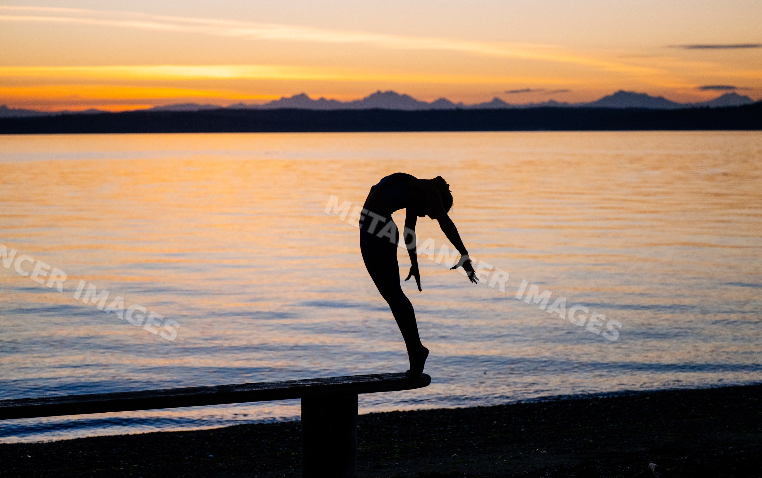 Hispanic woman balancing in acrobatic yoga pose on bench at lakeside