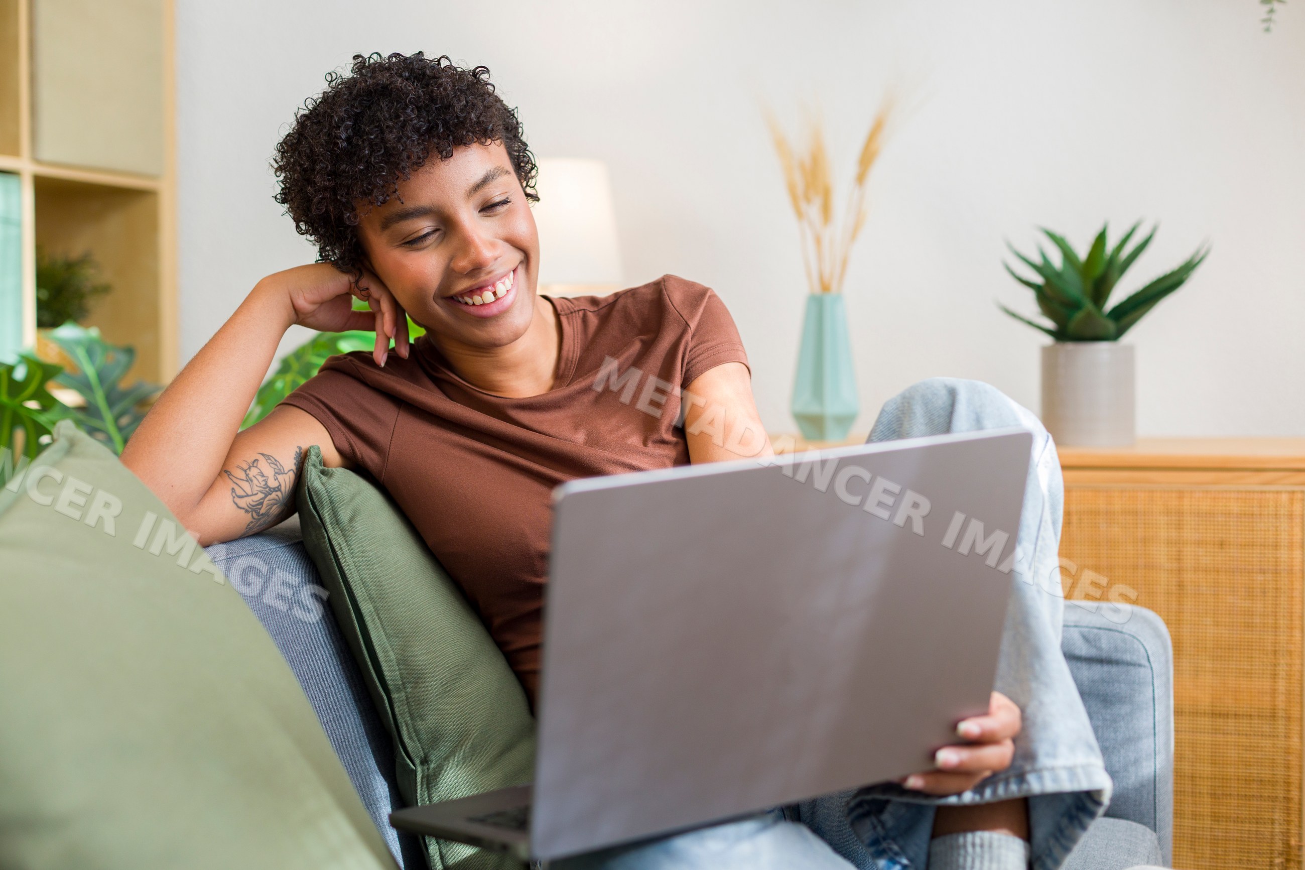 Young African American woman sitting on couch using laptop