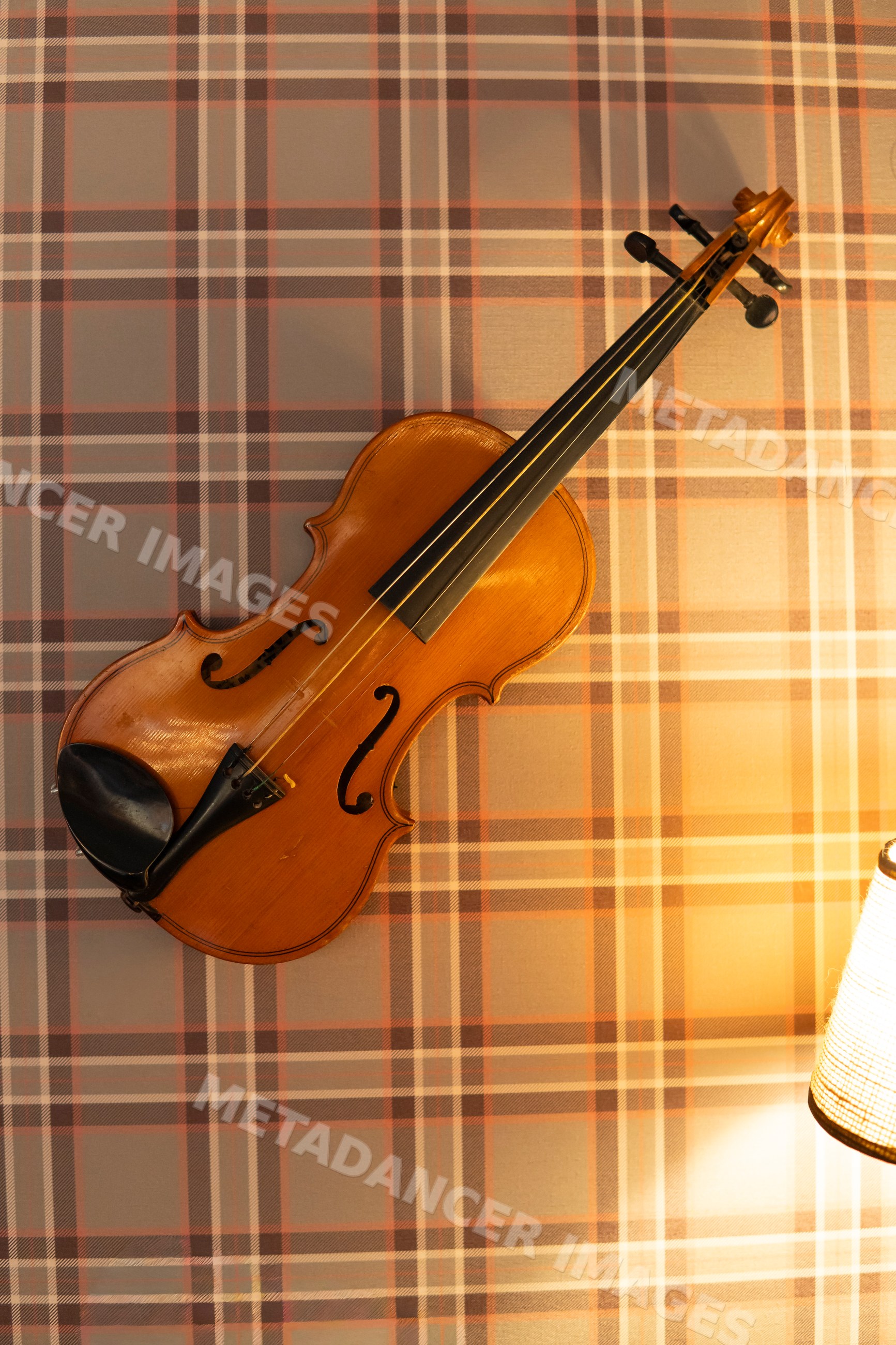 Wooden violin hanging on orange plaid wall with retro lamp