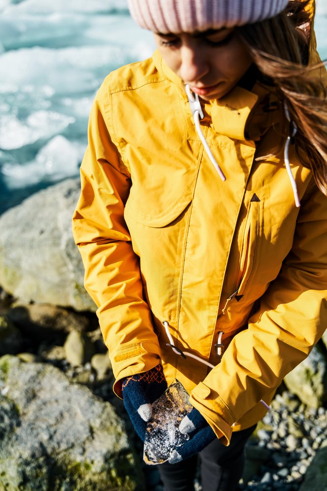 A white woman holds a piece of ice on a rocky shore