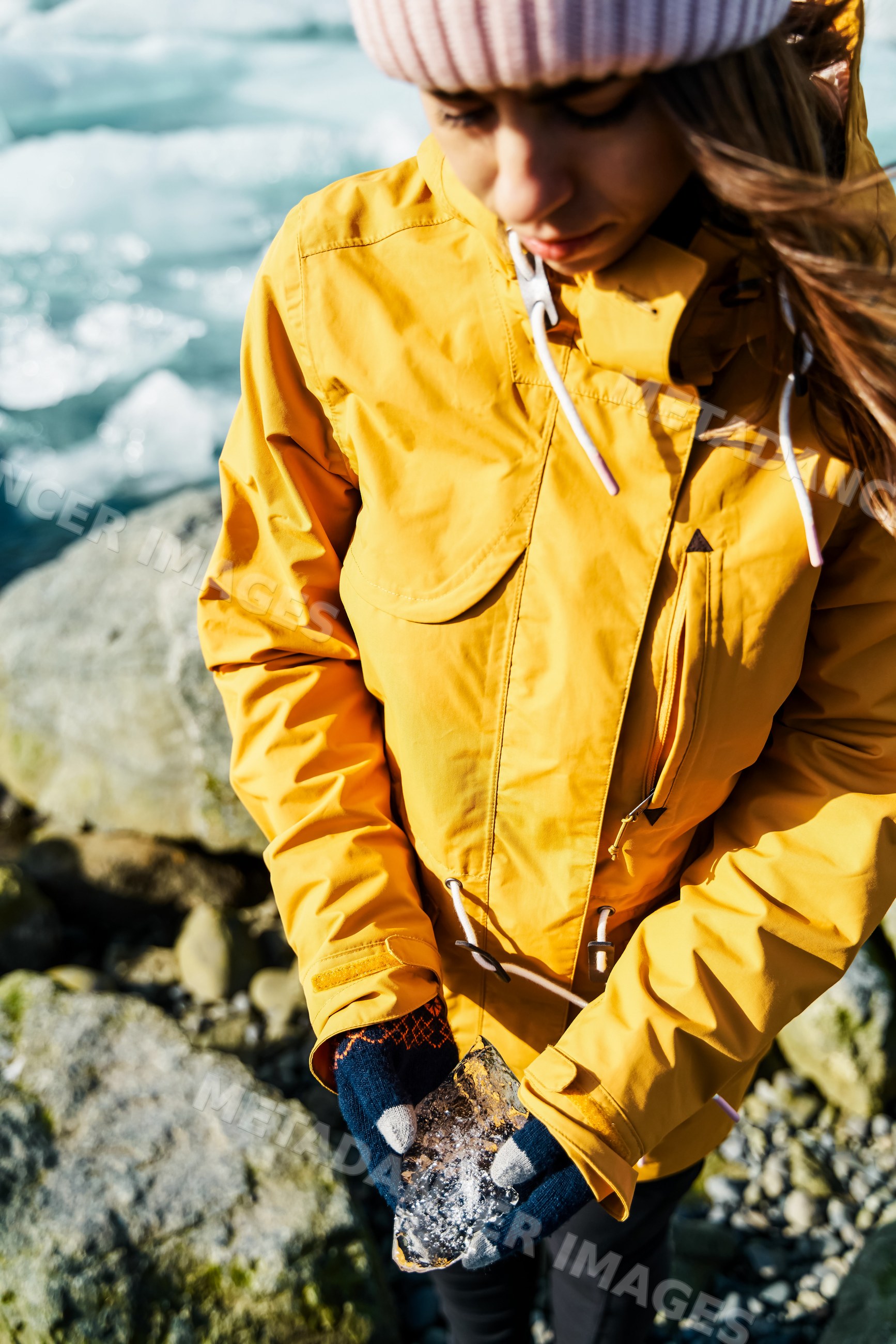 A white woman holds a piece of ice on a rocky shore