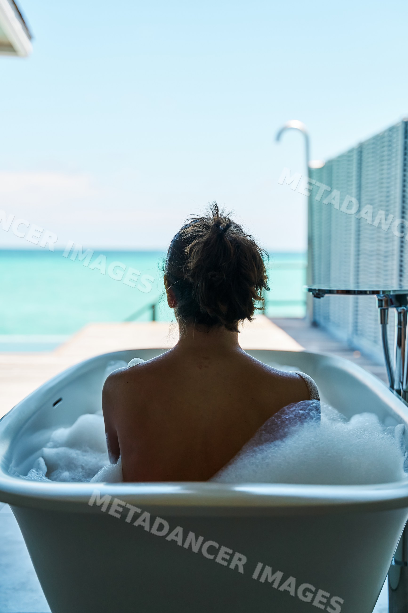 White Woman enjoying a bubble bath with ocean view